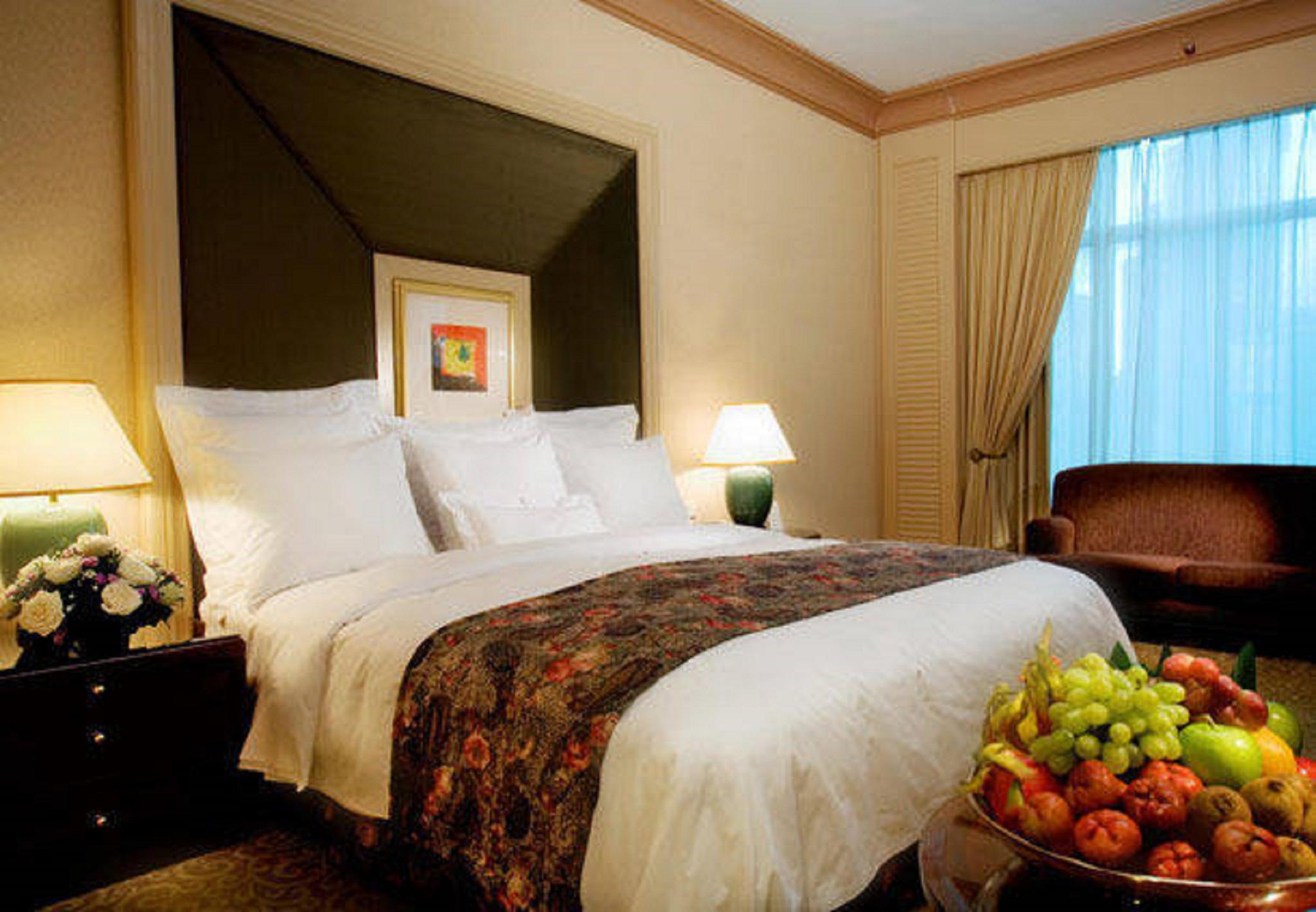 Отель Jw Marriott Куала-Лумпур Номер фото The photo shows a well-decorated hotel room. In the center, there is a large bed with white bedding and a decorative throw blanket featuring floral patterns. On either side of the bed, there are bedside tables with lamps. A comfortable armchair is po