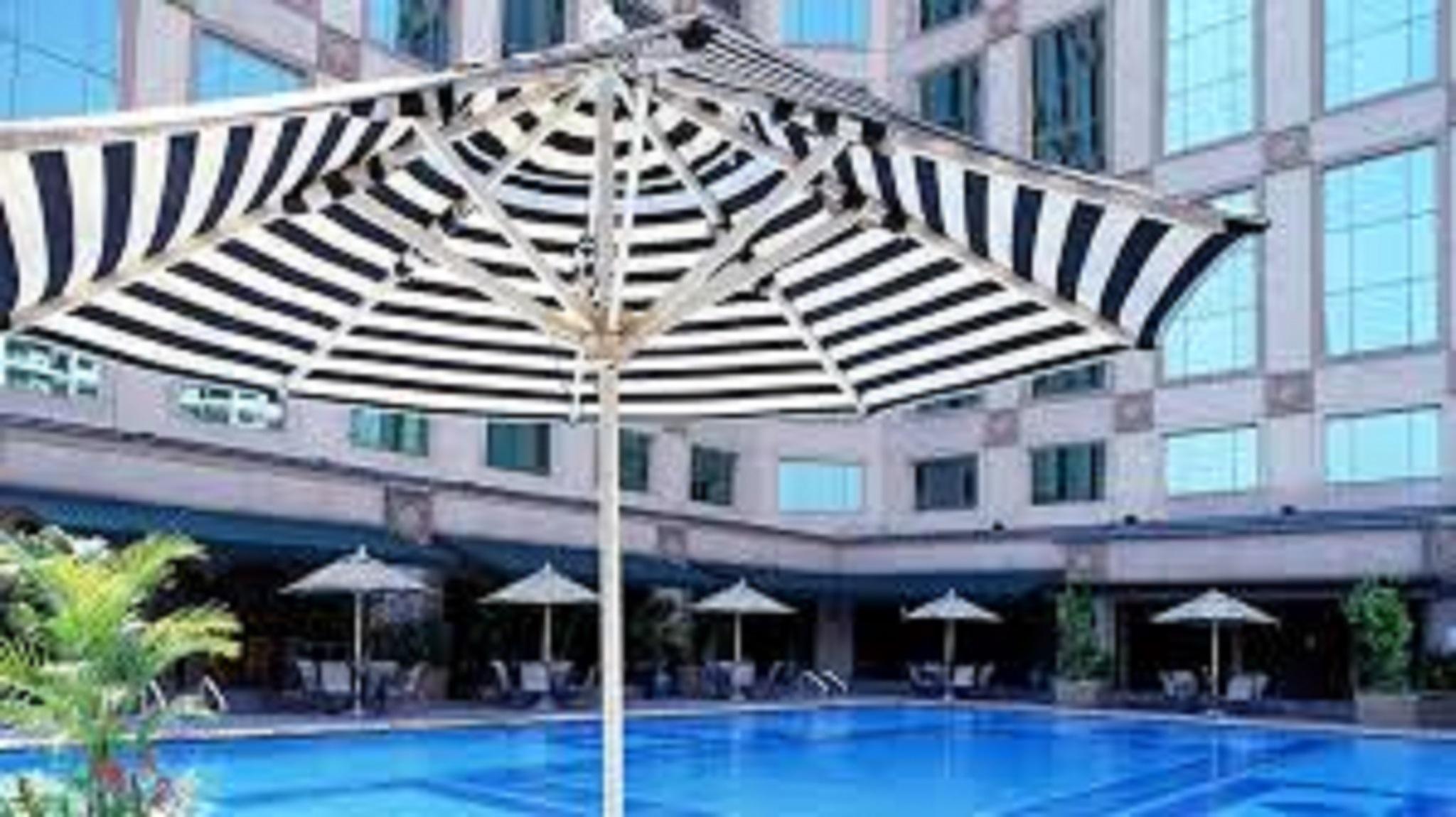 Отель Jw Marriott Куала-Лумпур Экстерьер фото The photo shows a swimming pool surrounded by a deck and several striped umbrellas providing shade. The pool has a clear blue water surface, and there are seating areas with lounges or chairs visible near the pool. The surrounding buildings have larg