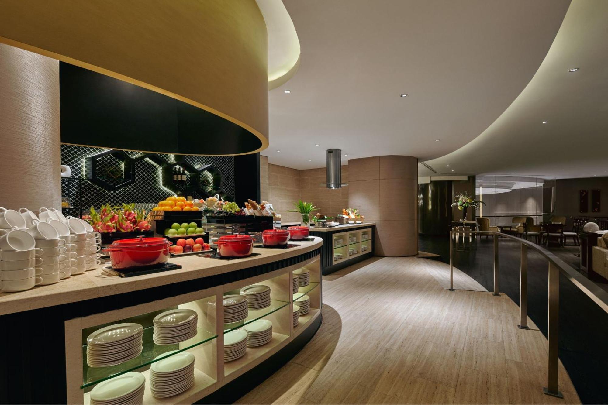 Отель Jw Marriott Куала-Лумпур Экстерьер фото The photo shows a stylish buffet area in a modern restaurant or hotel. There is a curved counter featuring a variety of food options, including fresh fruits and red bowls filled with dishes. Behind the counter, there are neatly arranged plates and a 