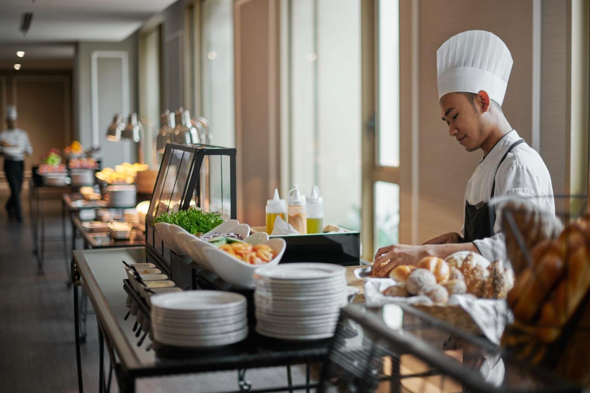 Отель Jw Marriott Куала-Лумпур Экстерьер фото The photo depicts a chef working in a buffet setting. He is wearing a chef's hat and uniform, focusing on preparing food. The buffet table is lined with a variety of dishes and ingredients, including salads and bread. There are several plates stacked