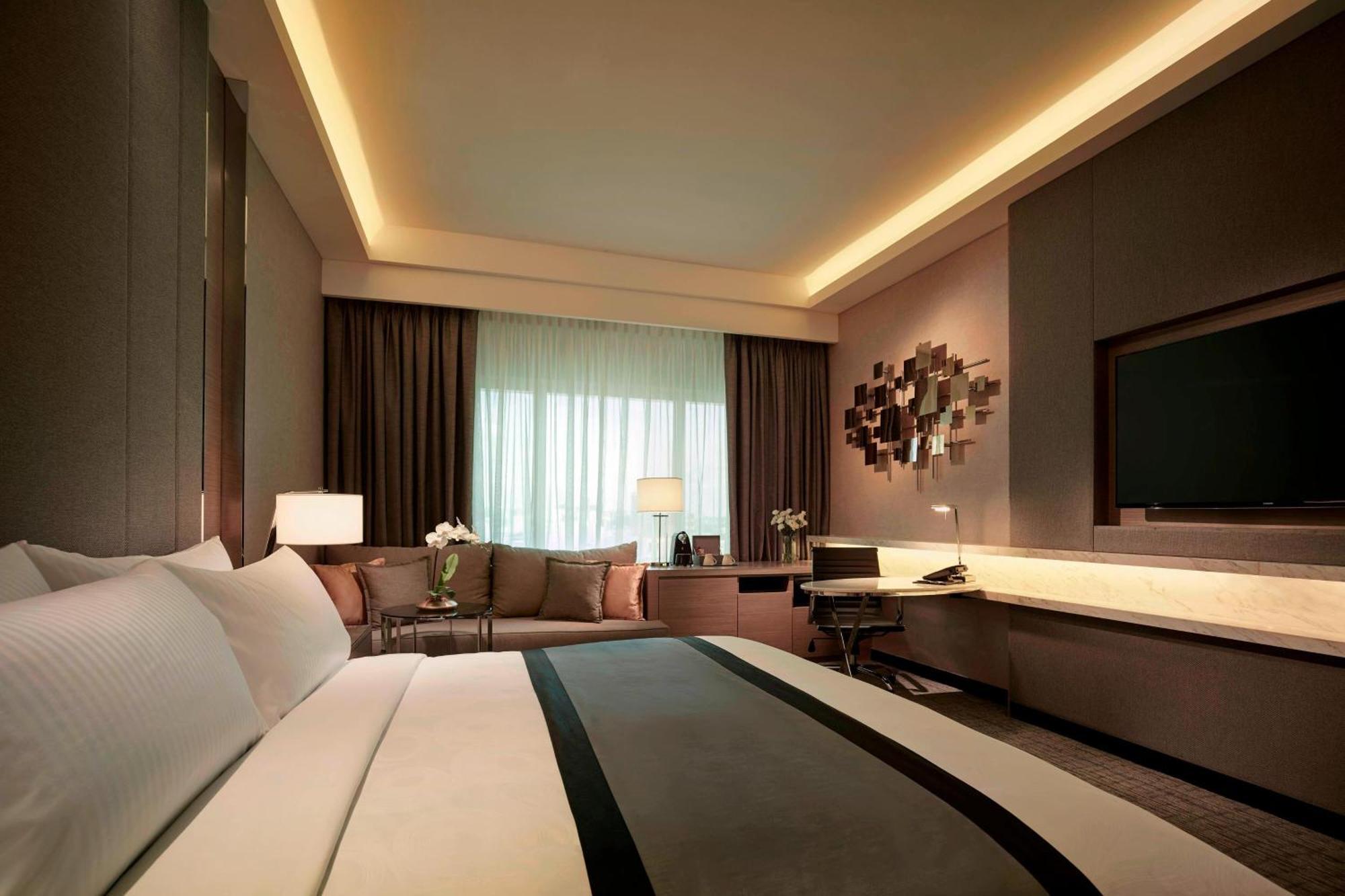 Отель Jw Marriott Куала-Лумпур Экстерьер фото The photo shows a modern hotel room with a sophisticated design. It features a large bed with crisp white linens and a decorative gray and black throw blanket. There are two bedside lamps providing soft lighting. In the background, there is a seating