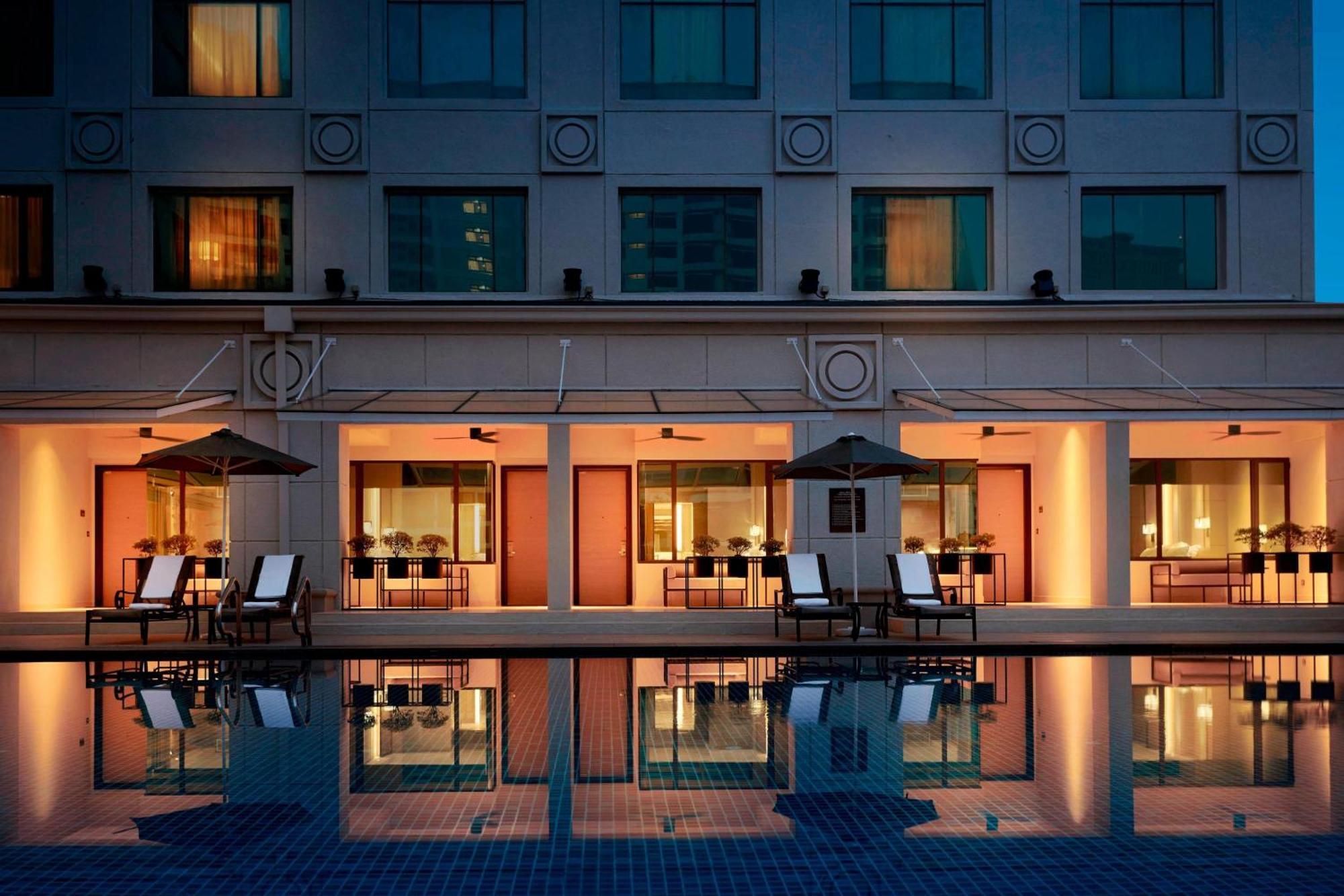 Отель Jw Marriott Куала-Лумпур Экстерьер фото The photo depicts a modern hotel or resort setting. In the foreground, there is a swimming pool with a blue tiled surface that reflects the surrounding architecture. In the background, the building features large windows, with warm lighting glowing f