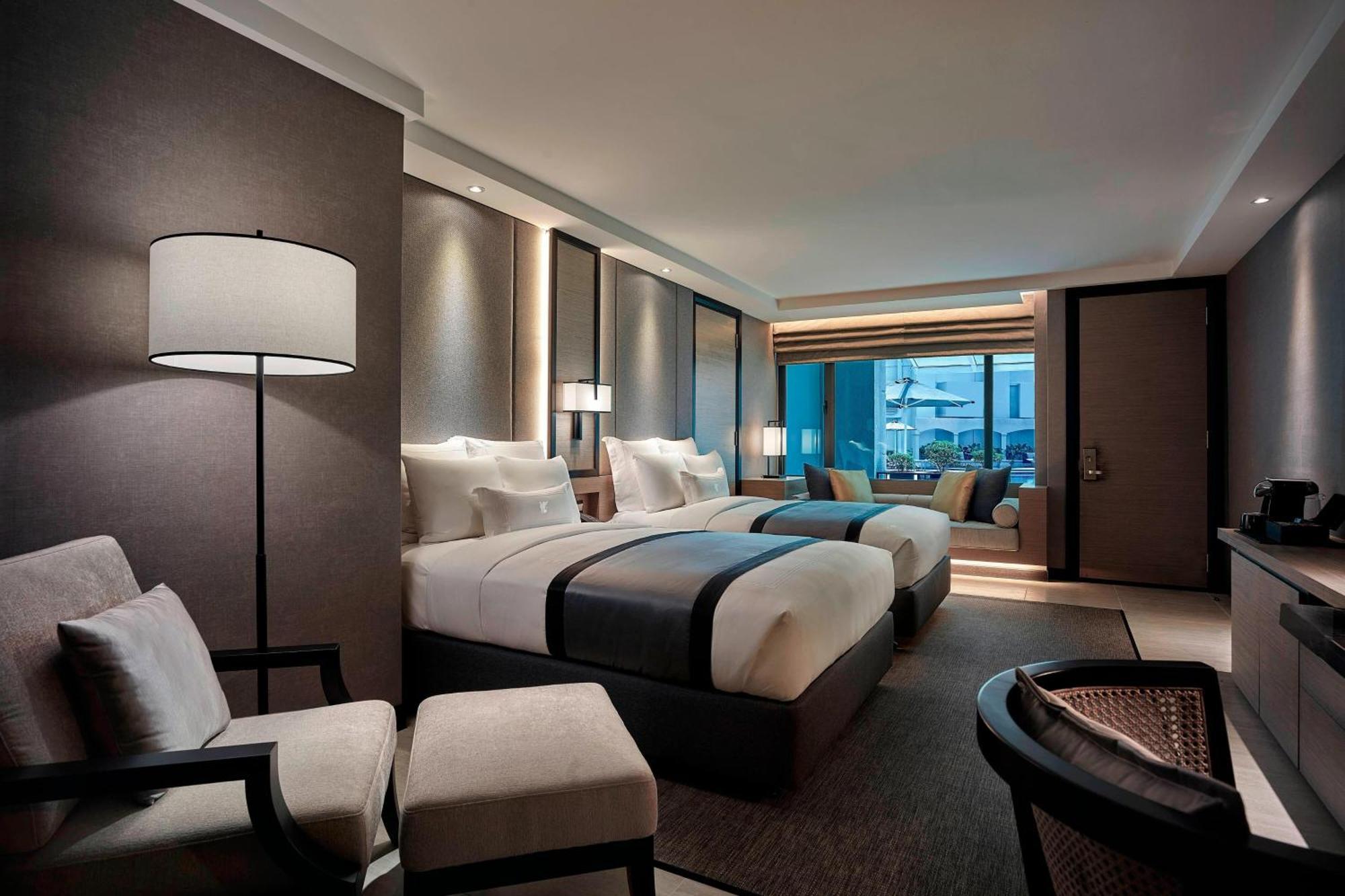 Отель Jw Marriott Куала-Лумпур Экстерьер фото The photo shows a modern hotel room with two beds featuring a sleek design. The beds are dressed in white linens and dark accents. There are two armchairs with a small table beside them, creating a cozy seating area. A large window allows natural lig