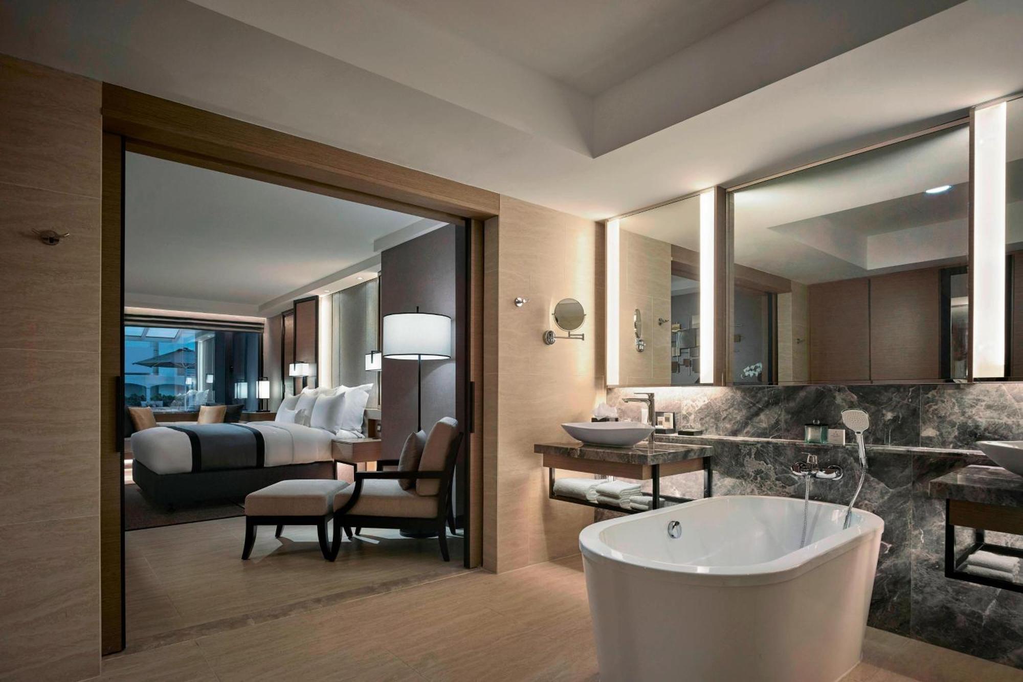 Отель Jw Marriott Куала-Лумпур Экстерьер фото The photo shows a luxurious hotel suite. In the foreground, there is a freestanding bathtub situated on a wooden floor. The bathroom area features modern fixtures, including a sink and a countertop made of dark stone. 

Through an open doorway, a wel