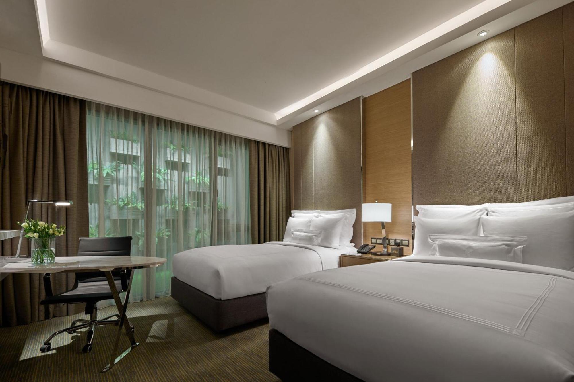 Отель Jw Marriott Куала-Лумпур Экстерьер фото The photo shows a modern hotel room featuring two beds with white bedding. The walls are styled with a combination of textured panels and soft lighting. There's a large window draped with sheer curtains, allowing natural light to enter the room. A sm