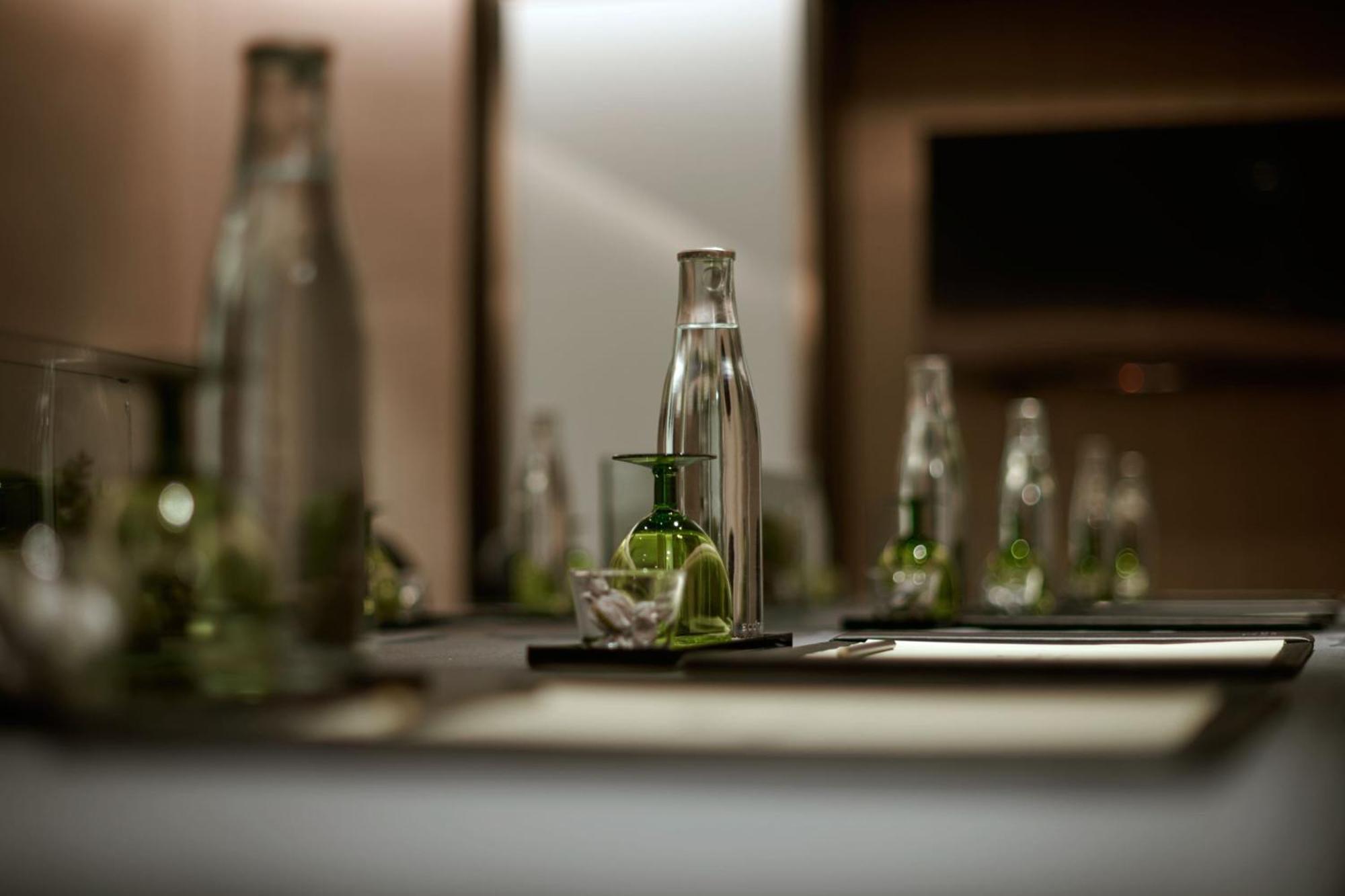Отель Jw Marriott Куала-Лумпур Экстерьер фото The photo shows a neatly arranged table setting, likely in a conference or dining room. It features several glass water bottles of various sizes, some of which are filled with water. In the center, there is a smaller glass container, possibly for hol