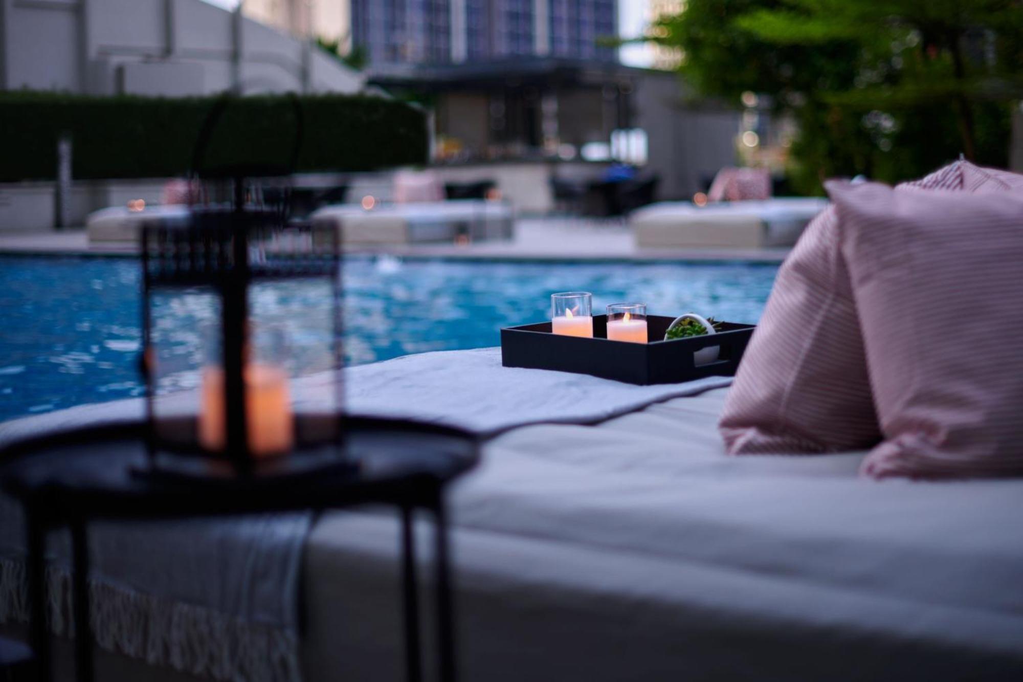 Отель Jw Marriott Куала-Лумпур Экстерьер фото The photo depicts a serene setting by a pool. In the foreground, there is a table with a lantern and candles, creating a cozy atmosphere. A tray on a lounge area holds three glasses and some greenery. Soft pillows add comfort, and the pool reflects t