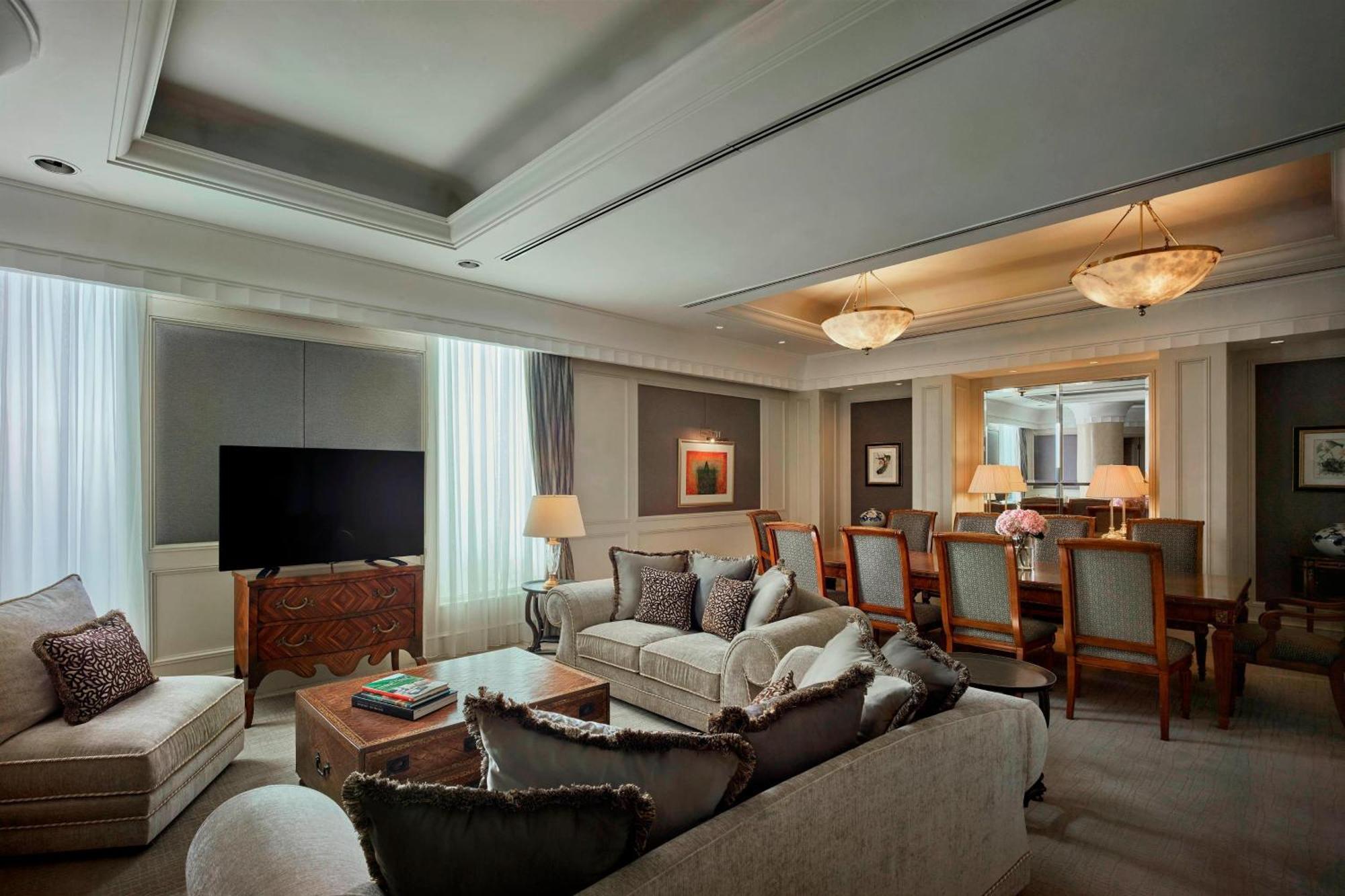 Отель Jw Marriott Куала-Лумпур Экстерьер фото The photo depicts a sophisticated living room. It features a comfortable beige couch with decorative pillows and a wooden coffee table, which has some books on it. To the left, there's a large television mounted on a wall. Natural light filters in th