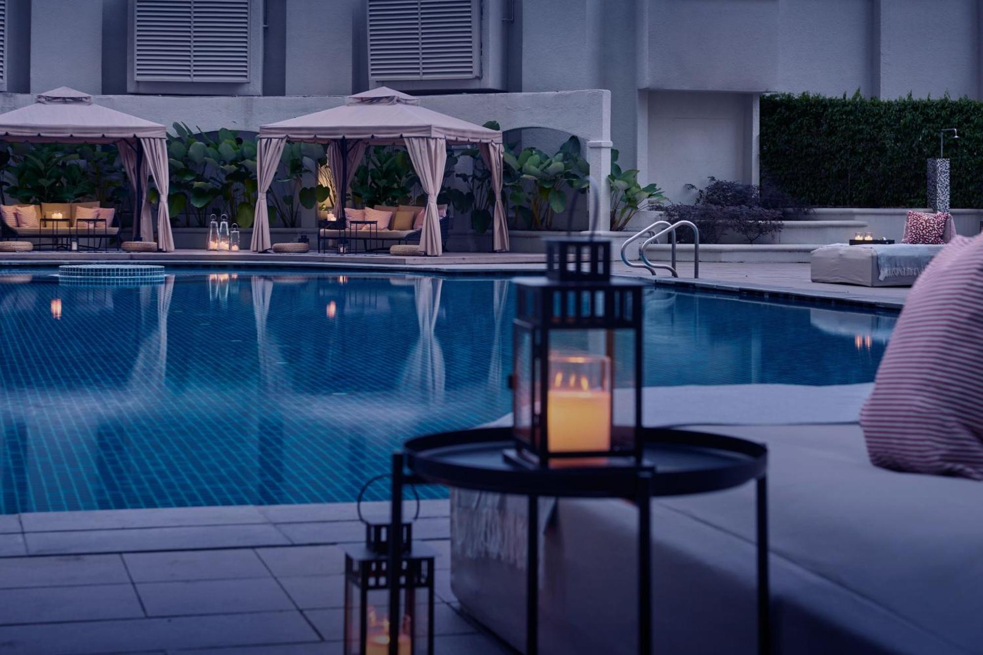 Отель Jw Marriott Куала-Лумпур Экстерьер фото The photo depicts a luxurious outdoor area featuring a swimming pool. Surrounding the pool are elegant cabanas with soft fabric drapes. The atmosphere is tranquil and inviting, enhanced by soft lighting from lanterns placed on a nearby table. The poo