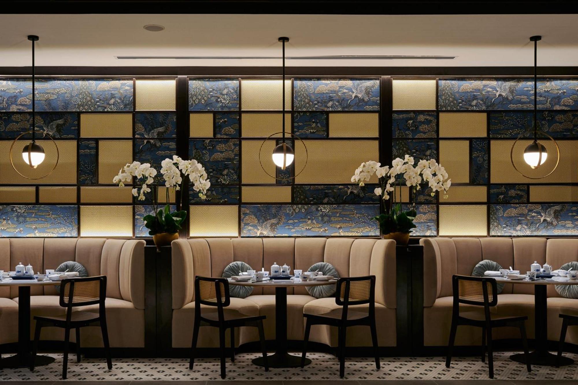 Отель Jw Marriott Куала-Лумпур Экстерьер фото The photo shows an elegant restaurant interior. The design features a stylish, modern aesthetic with tufted beige banquettes along the walls and dark wooden chairs. There are small round tables set with dishes and blue-and-white tableware. The backdr