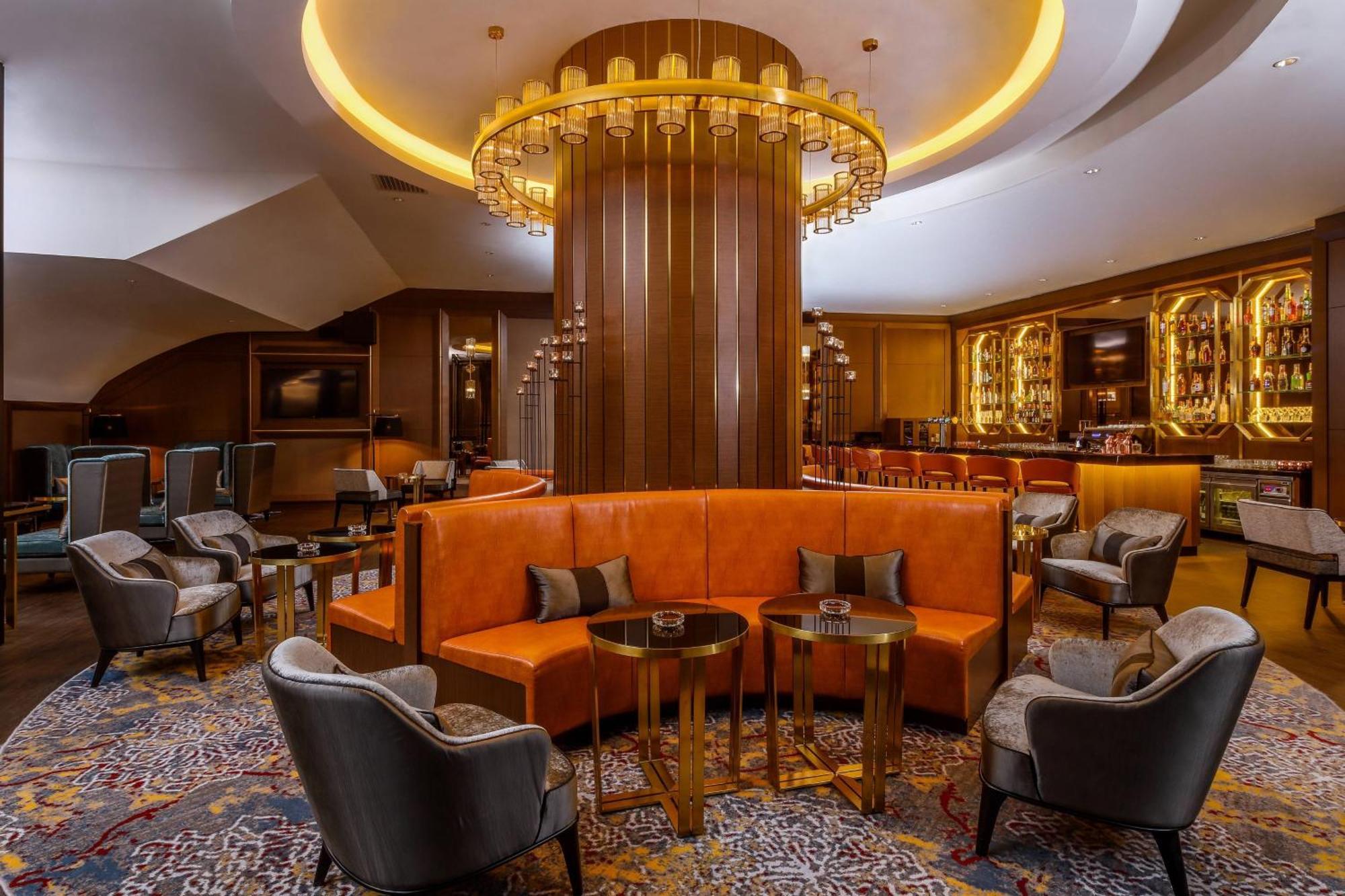 Отель Jw Marriott Куала-Лумпур Экстерьер фото The photo depicts a stylish and modern lounge area. At the center, there is a large, circular fixture with pendant lighting hanging from the ceiling, creating an elegant atmosphere. Surrounding this centerpiece are cozy seating arrangements, includin
